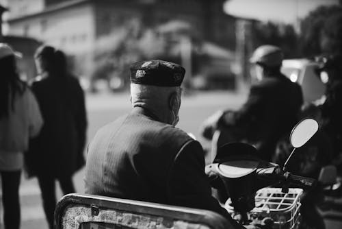 Grayscale Photo of Man in Black Suit Jacket and Black Hat Sitting on Motorbike