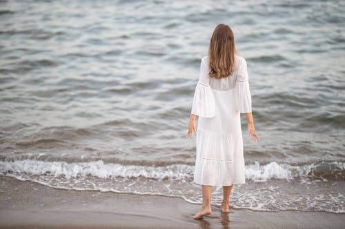 Free A Woman in a White Dress Standing at the Beach Stock Photo