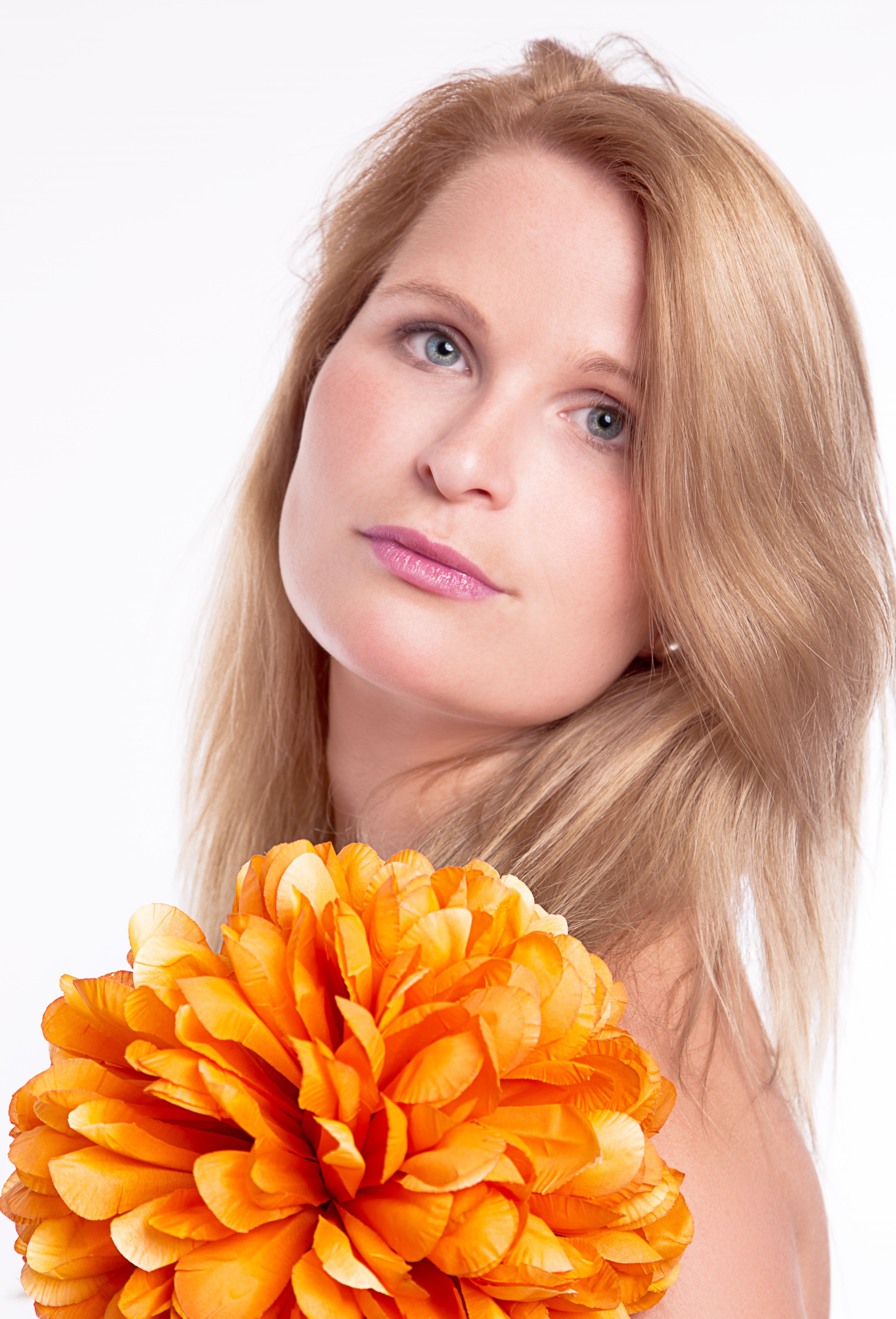 Elegant portrait of a blonde woman holding a vibrant orange flower against a light background.