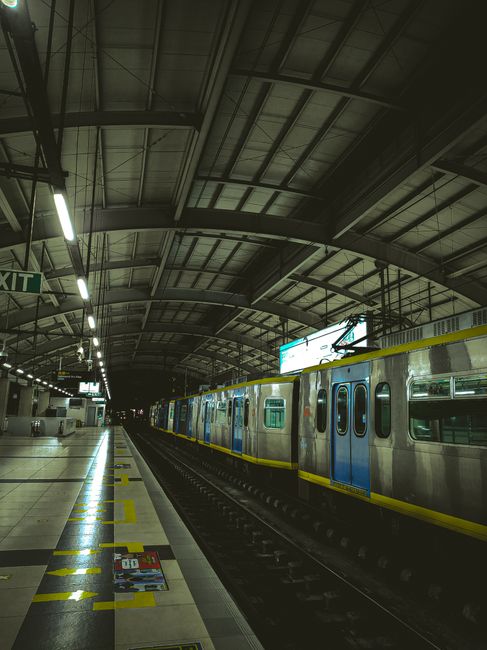 Interior of indoors contemporary railway station under arched ceiling with electric lights and modern train