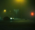 一辆轿车在雾蒙蒙的十字路口，借着红绿灯的光亮在夜间行驶