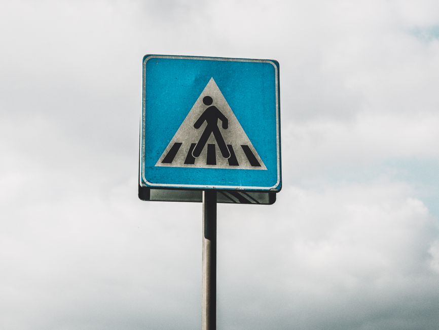 A blue pedestrian crossing sign stands against a cloudy sky in Italy.