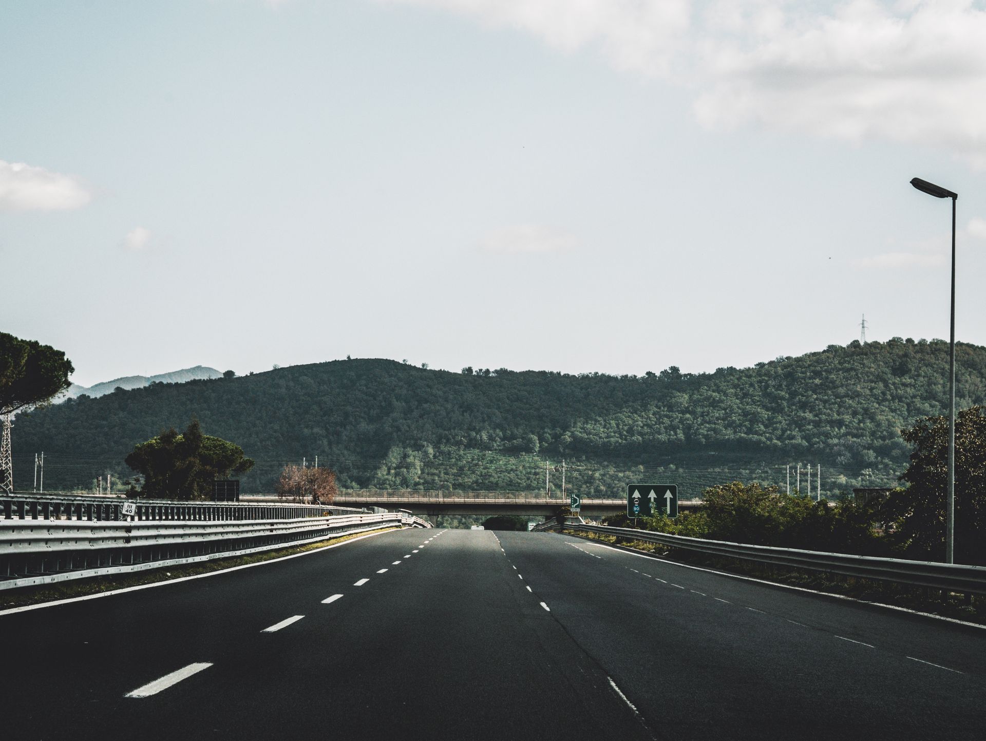 Peaceful highway cutting through lush Italian hills under a clear sky.