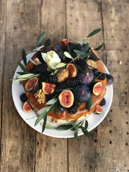 A delectable fig cake topped with fresh fruits and foliage on a rustic wooden table.