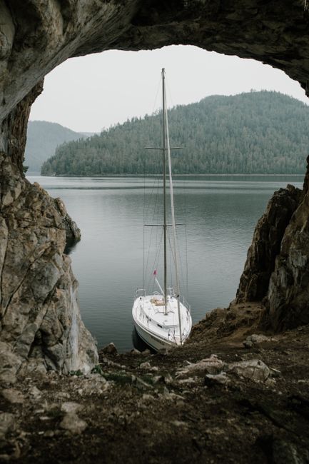 Sailboat docked in a serene river setting, framed by geological rock formations.