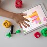 A child's hands interact with a block-based coding application on a digital tablet, surrounded by colorful cube toys.