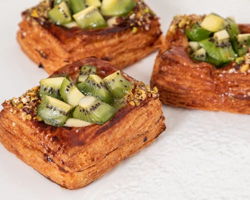 Closeup of golden baked puff pastries with glazed kiwi cubes and crushed nuts