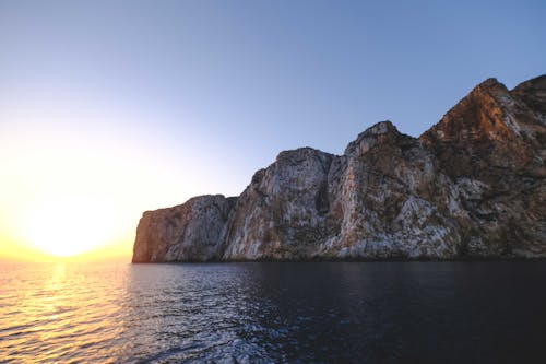 Picturesque view of high dry mount against rippled ocean with horizon under glowing sun in twilight