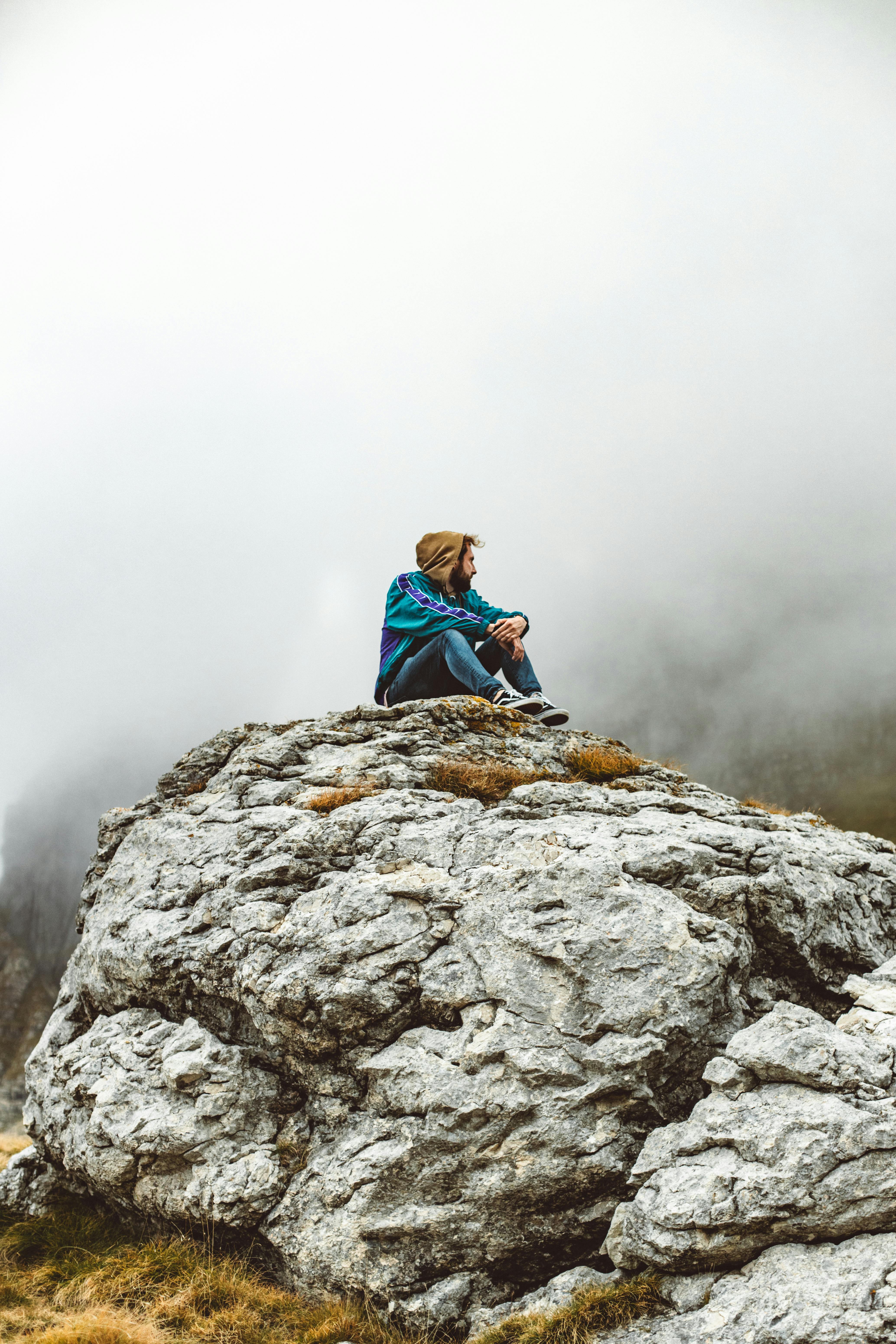 a man wearing jacket sitting on the rock