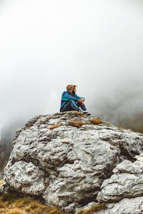 Free A young man contemplates atop a rocky mountain with a foggy backdrop, capturing the essence of solitude and nature. Stock Photo