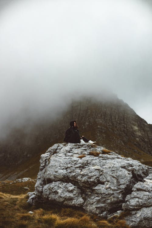 Person Sitting on a Rock during Foggy Weather