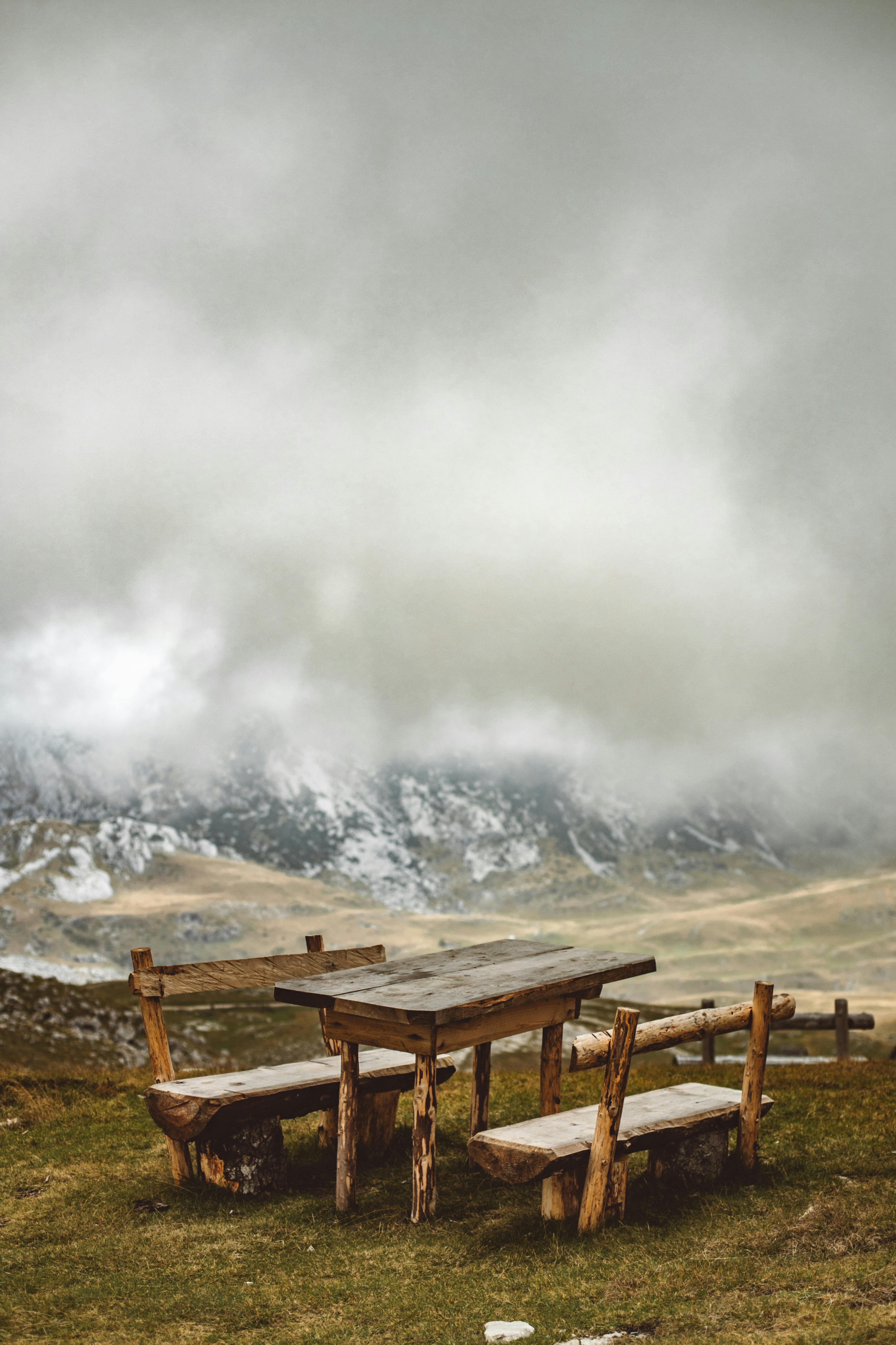 雾气缭绕的山区前，一张木凳背靠而立，营造出宁静而美丽的自然氛围