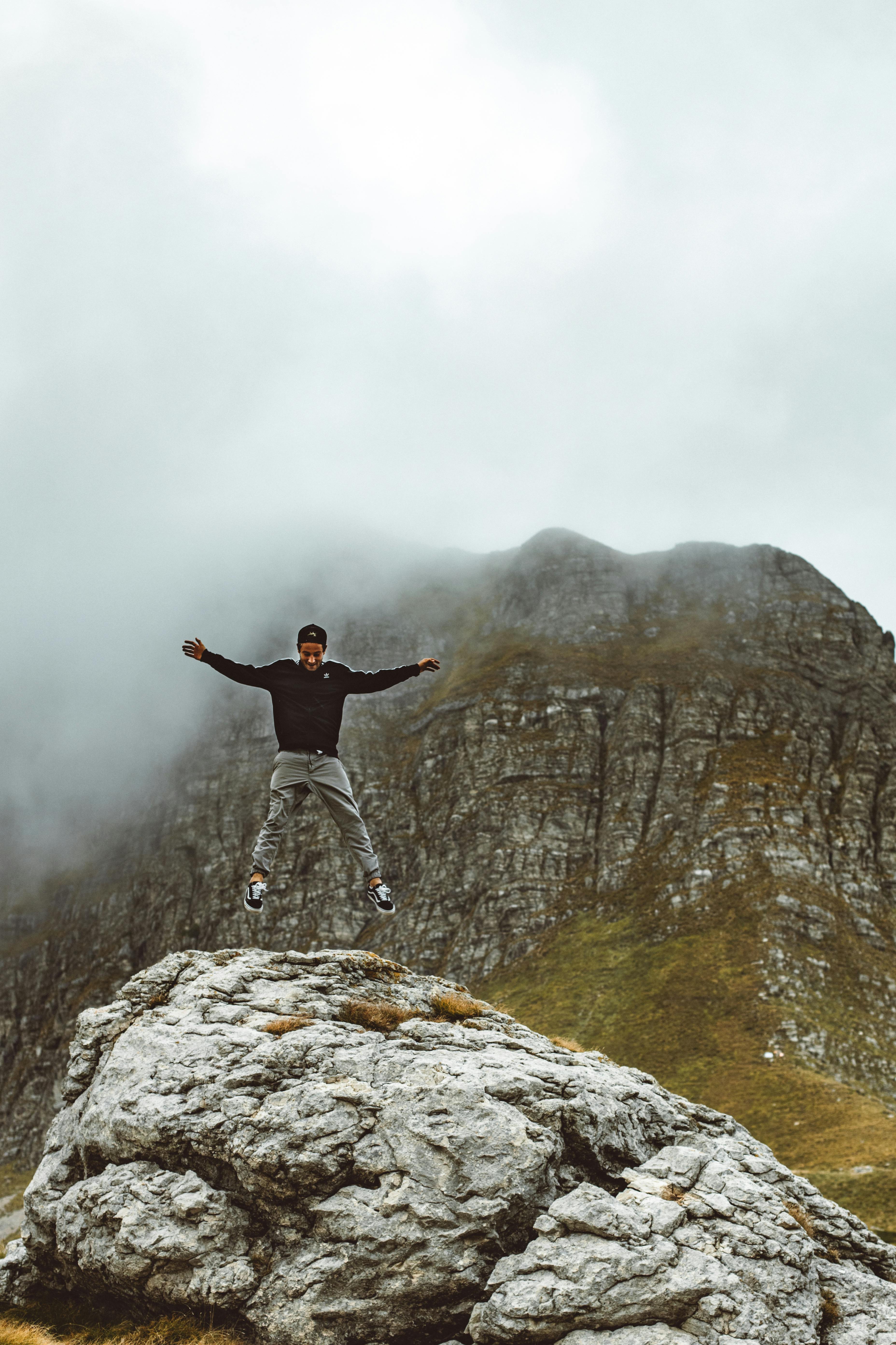 man in black jacket on mid air over a boulder