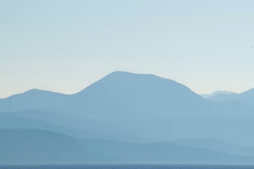 Mystic view of massive rough mountain range covered with thick mist under blue sky