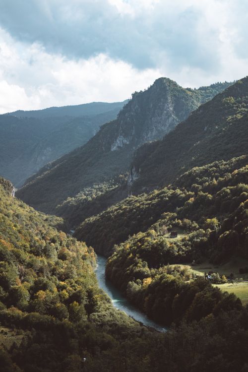 Free Peaceful mountain landscape with a winding river and lush greenery under a cloudy sky. Stock Photo