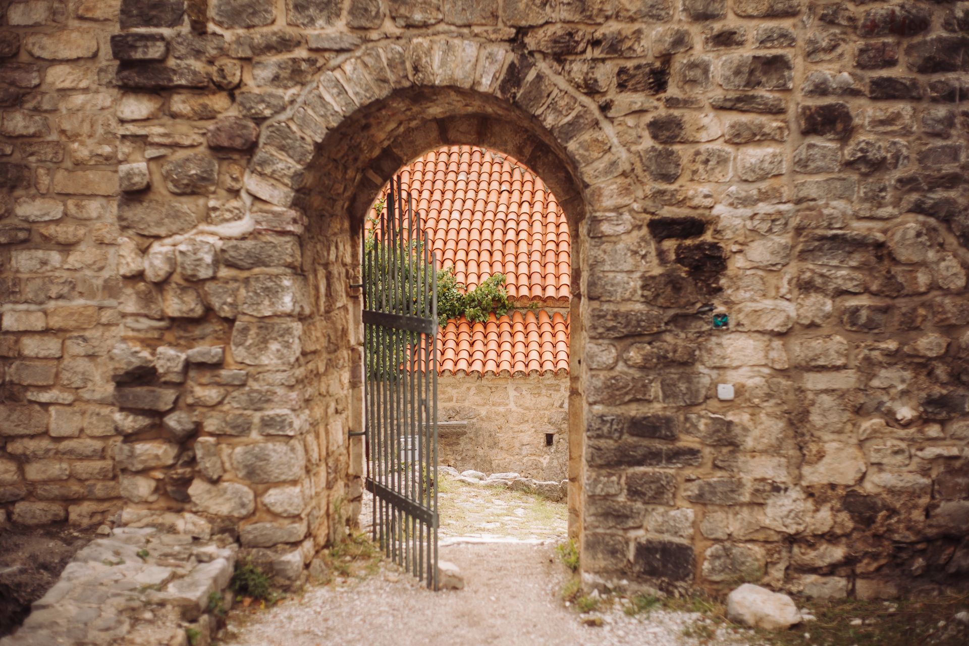 A rustic stone archway leads to a charming courtyard with tiled roof.