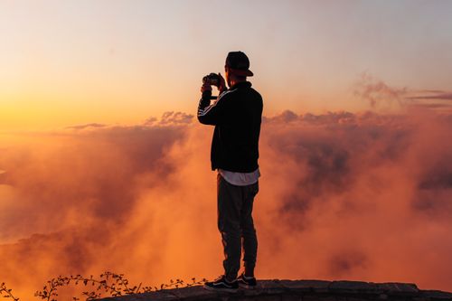 Free A person takes a photo of a stunning sunset with clouds from a hilltop. Stock Photo