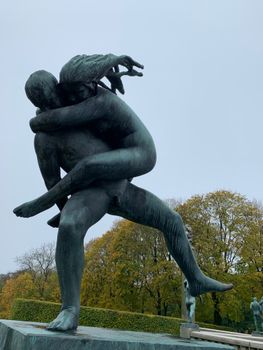 Dramatic stone sculpture of a couple embracing located in a lush outdoor park.