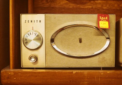 Close-up of a vintage Zenith radio with a sale tag on a wooden shelf, showing dials and speaker design.
