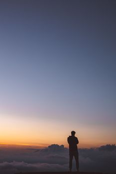 一名男子站在那里，身后是充满活力的日落、云层和广阔的天空