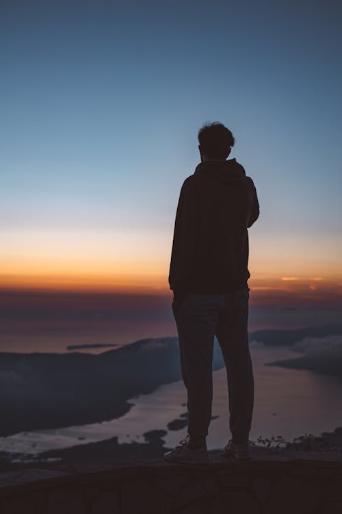 Man in Black Jacket Standing on Top of Mountain during Sunset