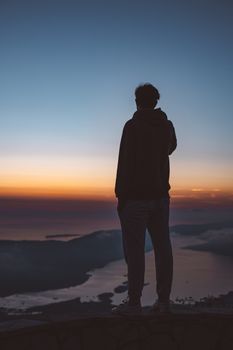 日落时分，一名男子站在山顶，俯瞰着美丽的海岸景色