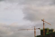 Bright high cranes near urban house during construction under cloudy sky in daylight