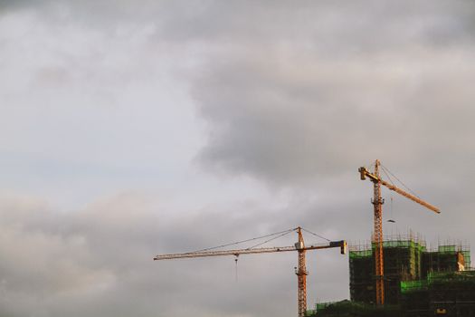 Bright high cranes near urban house during construction under cloudy sky in daylight