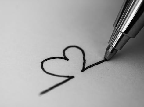 A monochrome close-up of a pen drawing a heart on paper, symbolizing love or creativity.