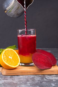 Vibrant beetroot and orange juice blend being poured in a glass with fresh garnish on a wooden board.