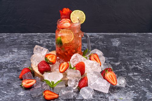 Free Chilled strawberry lemonade with lime in a mason jar surrounded by ice and fresh strawberries. Stock Photo