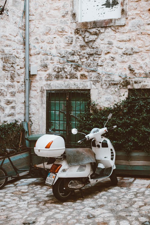 White Motor Scooter Parked Beside Brown Stone Wall