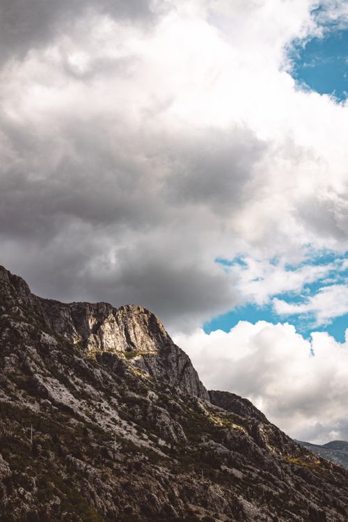 Free Vertical shot of rugged rocky cliffs under dramatic clouds and blue sky, capturing the essence of nature. Stock Photo