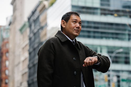 Elegant ethnic businessman checking time on wristwatch on city street