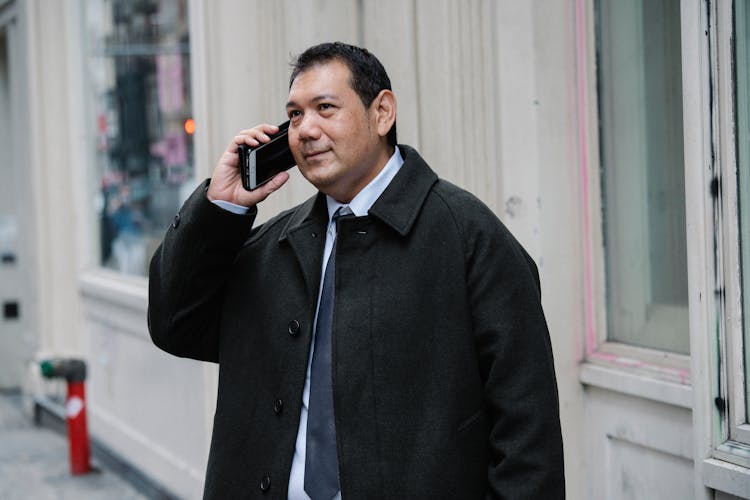 Well Dressed Ethnic Businessman Talking On Smartphone Near Aged Building