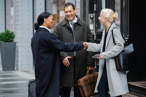 Positive diverse colleagues shaking hands after meeting on street