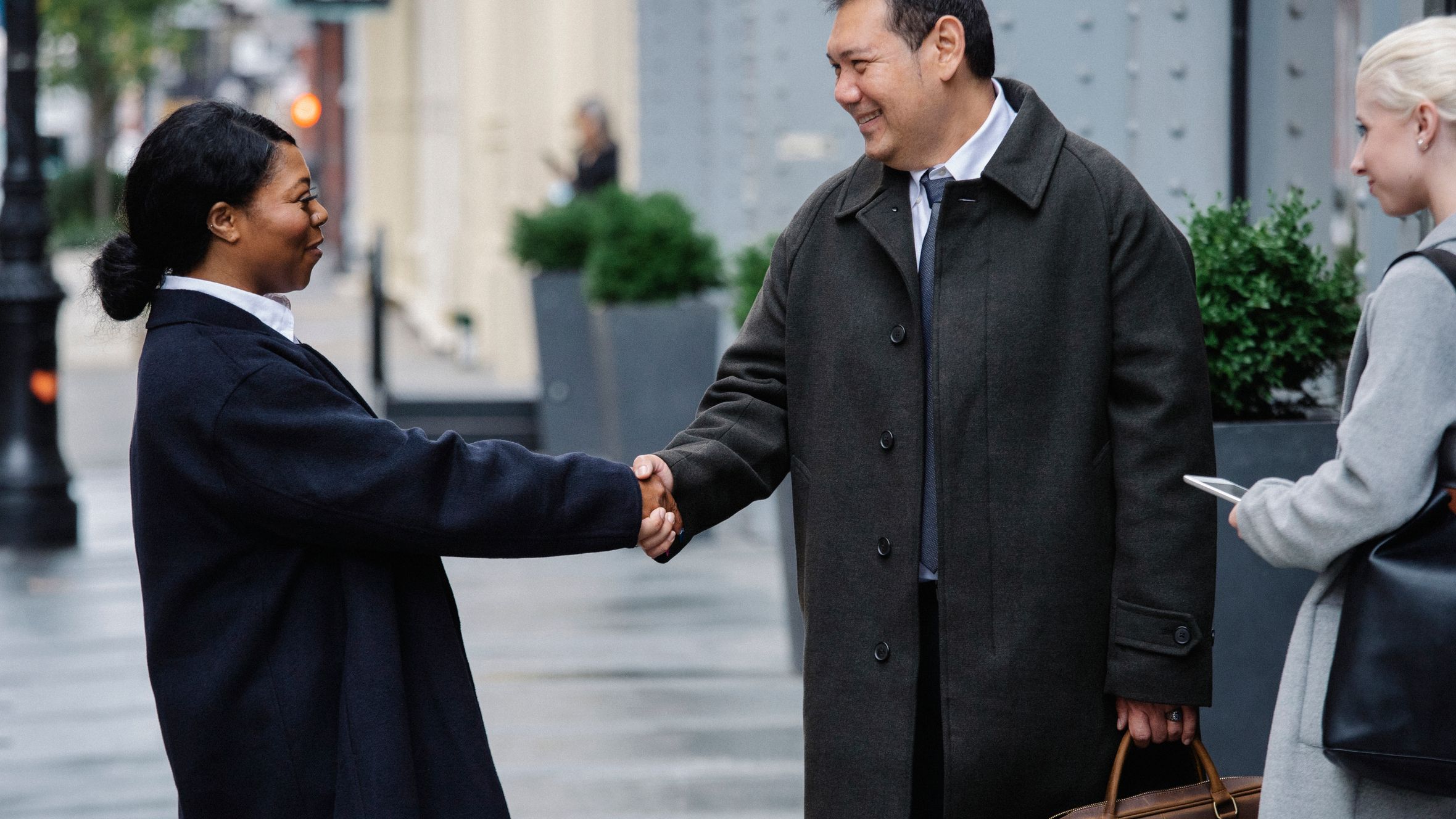 Side view of positive young African American woman in classy outfit shaking hand of smiling ethnic male partner while standing on city street after business meeting