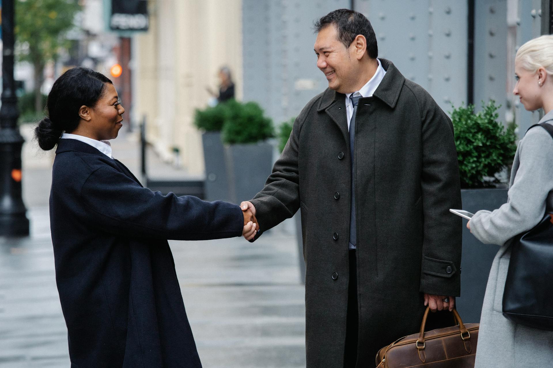 Side view of positive young African American woman in classy outfit shaking hand of smiling ethnic male partner while standing on city street after business meeting