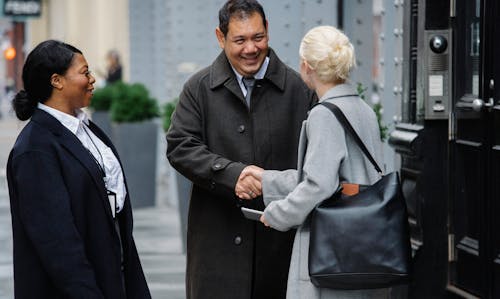 Positive ethnic colleagues greeting anonymous female partner on street