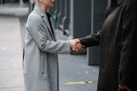 Crop anonymous man and woman in elegant coats shaking hands on street while having meeting in city downtown