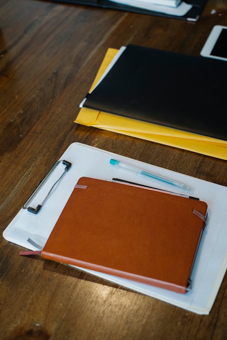 Notebook And Clipboard With Papers Placed On Desk With Folders And Pens