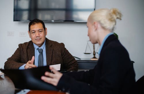 Young female employee with blond hair in classy suit representing project details to middle aged ethnic male manager while working together in office