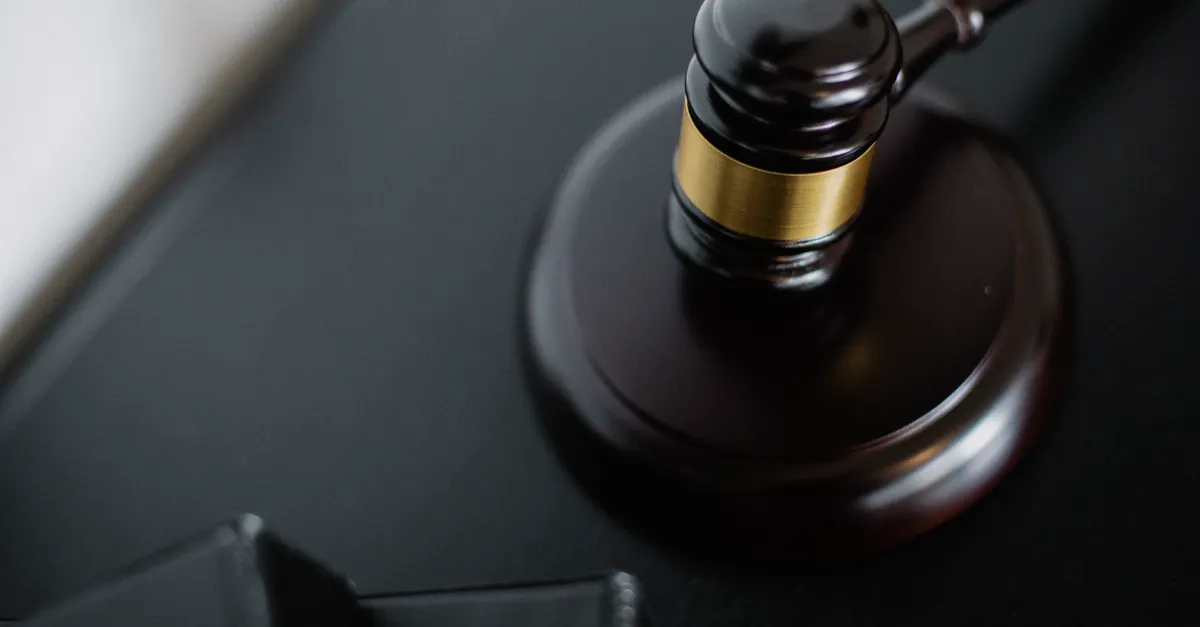 A wooden gavel on a round surface beside case folders in a courtroom