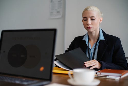 Free Serious young woman in formal clothes sitting at table and working with documents in office Stock Photo
