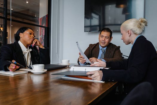 Multiethnic coworkers in formal wear sitting at table with documents and discussing details of business project