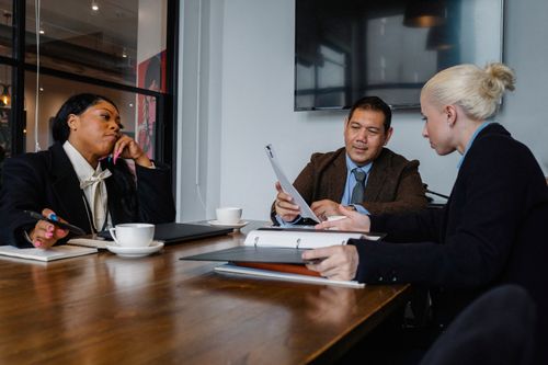 Free Multiethnic coworkers in formal wear sitting at table with documents and discussing details of business project Stock Photo