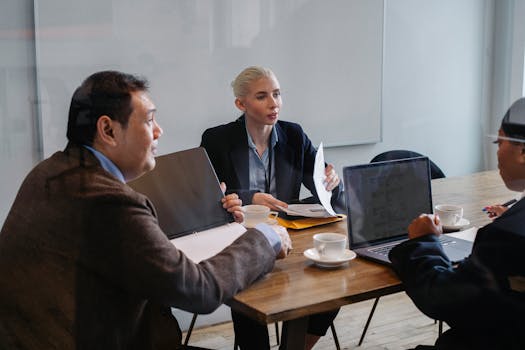 Multiracial colleagues in formal clothes sitting at table with laptop and documents while discussing details of business plan