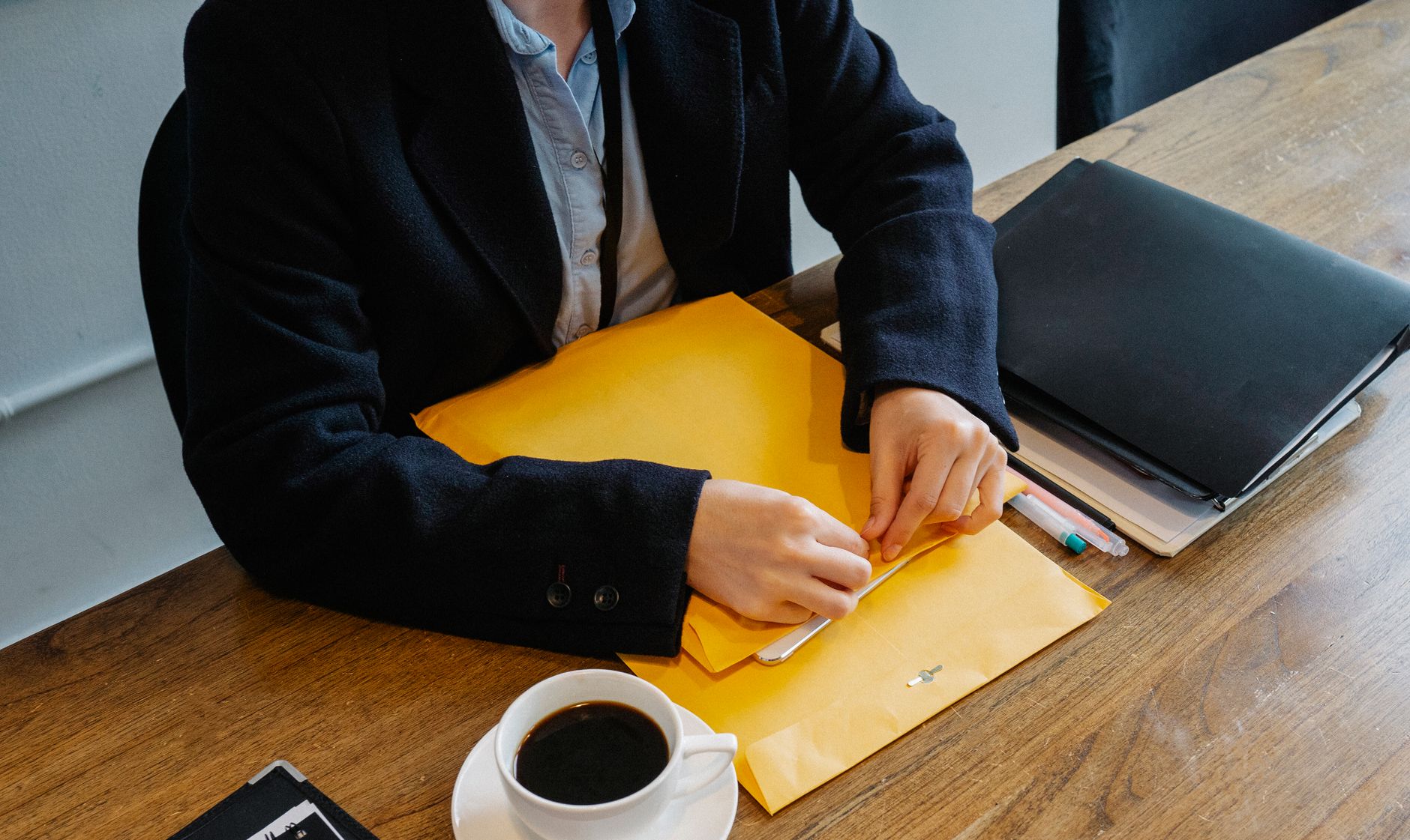High angle of crop faceless female in formal clothes sitting at wooden table with coffee and documents while having break in workplace