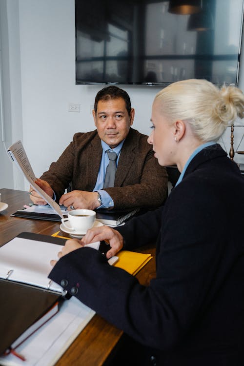 Free Side view of serious woman in formal clothes sitting at table and discussing details of project with ethnic colleague Stock Photo