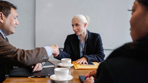 Group of diverse coworkers in formal suits shaking hands after successful business deal in office